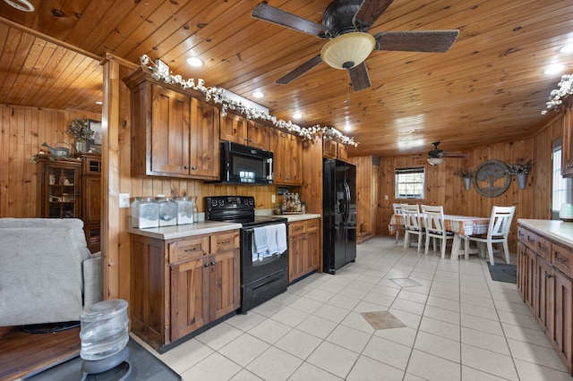 kitchen featuring light tile patterned flooring, wood ceiling, black appliances, and wooden walls