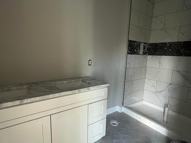 bathroom with tile patterned flooring, a tile shower, and vanity