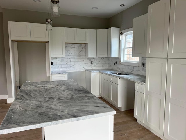 kitchen featuring hardwood / wood-style floors, decorative light fixtures, decorative backsplash, white cabinets, and a center island