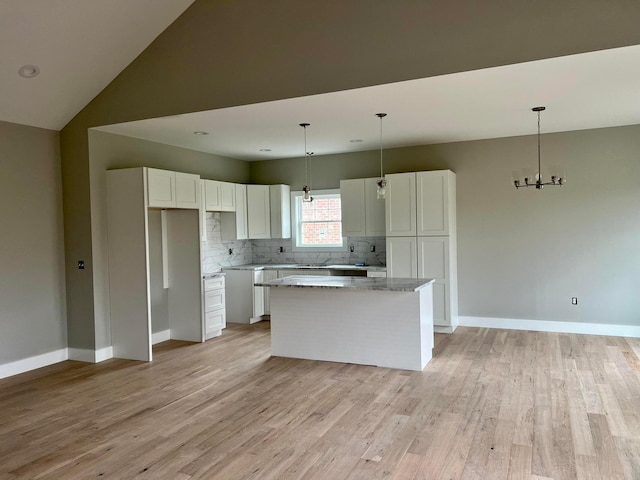 kitchen with light wood-type flooring, a kitchen island, light stone counters, lofted ceiling, and white cabinetry