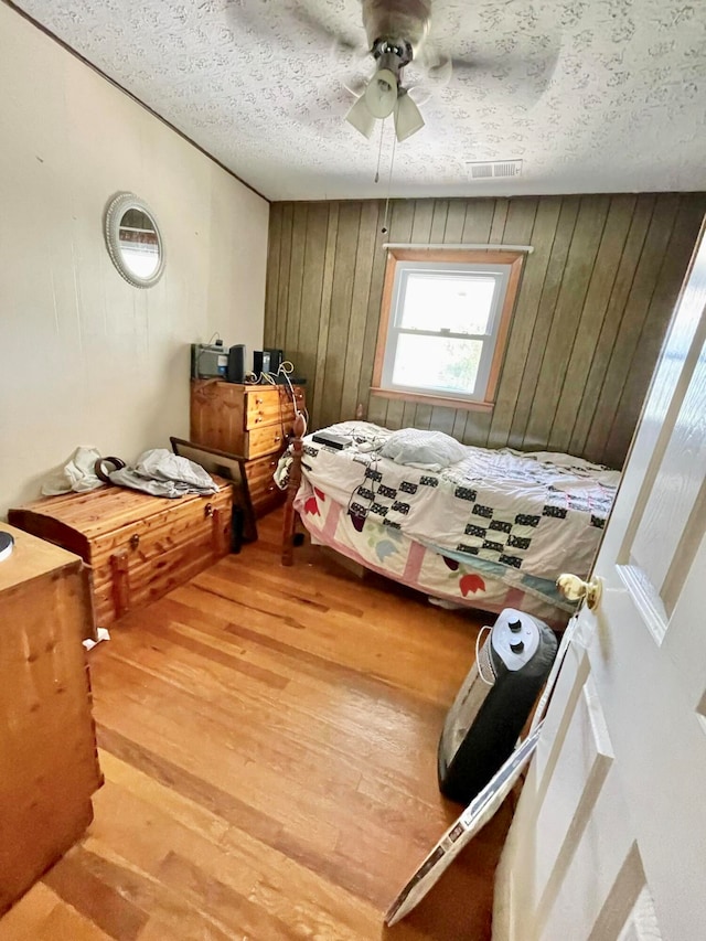 bedroom with ceiling fan, wood walls, hardwood / wood-style floors, and a textured ceiling