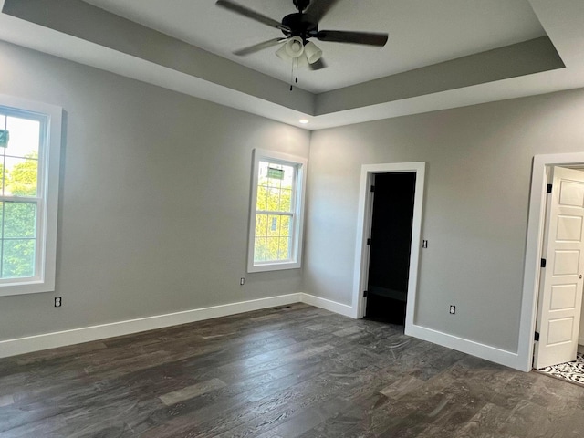 empty room with ceiling fan, a wealth of natural light, dark hardwood / wood-style floors, and a raised ceiling