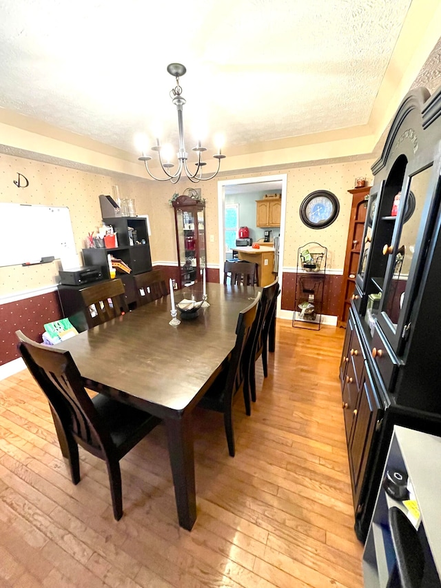 dining room with wooden walls, an inviting chandelier, light wood-type flooring, and a textured ceiling