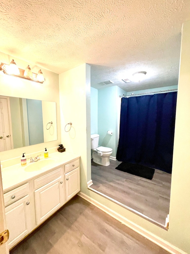 bathroom featuring vanity, a textured ceiling, hardwood / wood-style flooring, walk in shower, and toilet