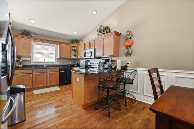 kitchen with lofted ceiling, stainless steel appliances, a breakfast bar, dark stone countertops, and light hardwood / wood-style floors