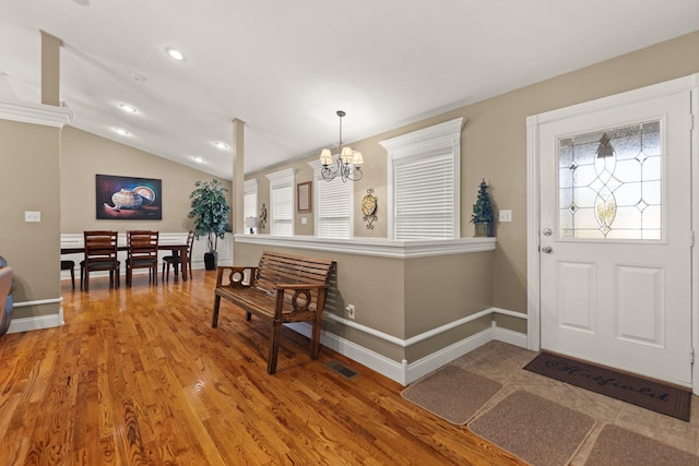 foyer entrance with wood-type flooring, a notable chandelier, and vaulted ceiling