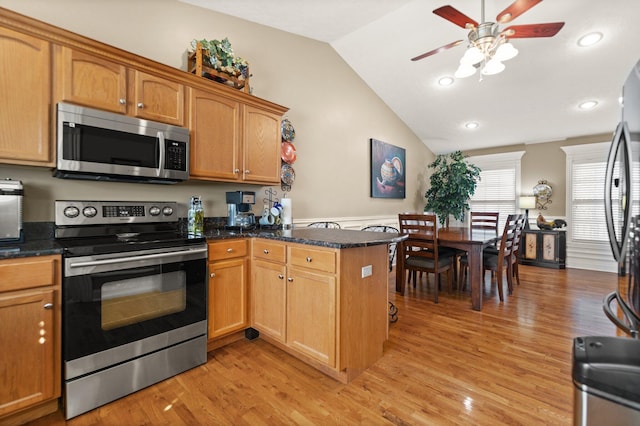 kitchen featuring light hardwood / wood-style floors, dark stone countertops, vaulted ceiling, kitchen peninsula, and appliances with stainless steel finishes