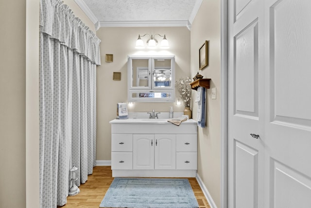 bathroom with vanity, baseboards, a textured ceiling, crown molding, and wood finished floors