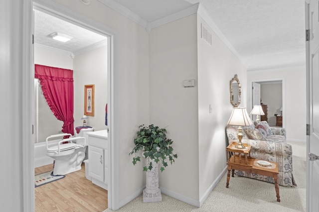 hall featuring a textured ceiling, ornamental molding, visible vents, light wood finished floors, and baseboards