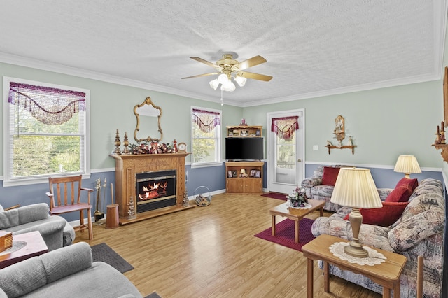 living room with a textured ceiling, wood finished floors, a ceiling fan, and a warm lit fireplace