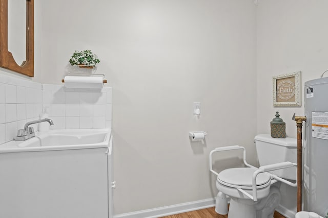 bathroom featuring toilet, wood finished floors, a sink, electric water heater, and baseboards