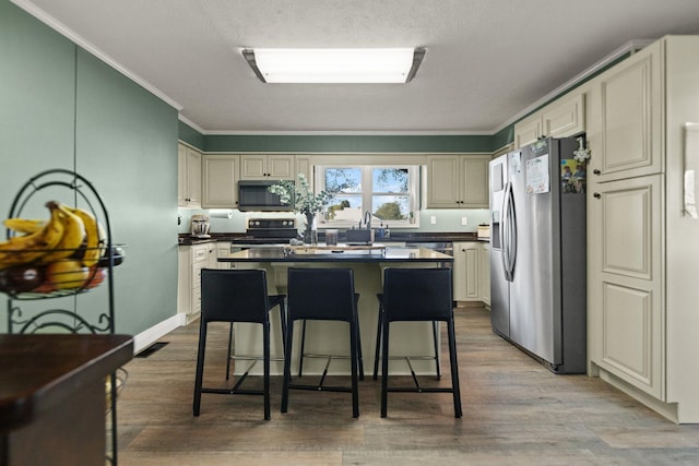 kitchen featuring cream cabinets, light wood-type flooring, crown molding, appliances with stainless steel finishes, and a center island