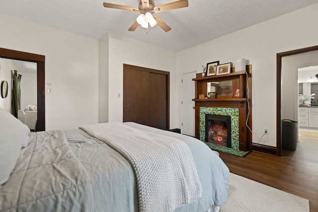 bedroom featuring ceiling fan, dark wood-type flooring, a closet, a stone fireplace, and connected bathroom