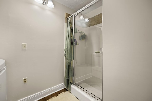 bathroom with hardwood / wood-style floors, a shower with shower door, a textured ceiling, and toilet