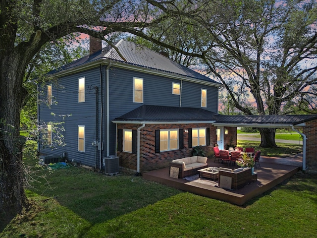 back house at dusk with outdoor lounge area, central AC unit, a lawn, and a patio area