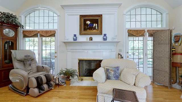 sitting room with vaulted ceiling, a tiled fireplace, light wood-type flooring, and plenty of natural light