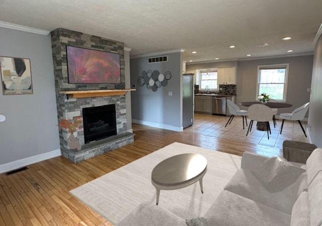 living room with sink, light hardwood / wood-style flooring, a stone fireplace, and crown molding