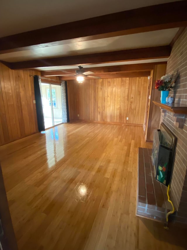 unfurnished living room featuring ceiling fan, beam ceiling, wooden walls, a fireplace, and hardwood / wood-style floors