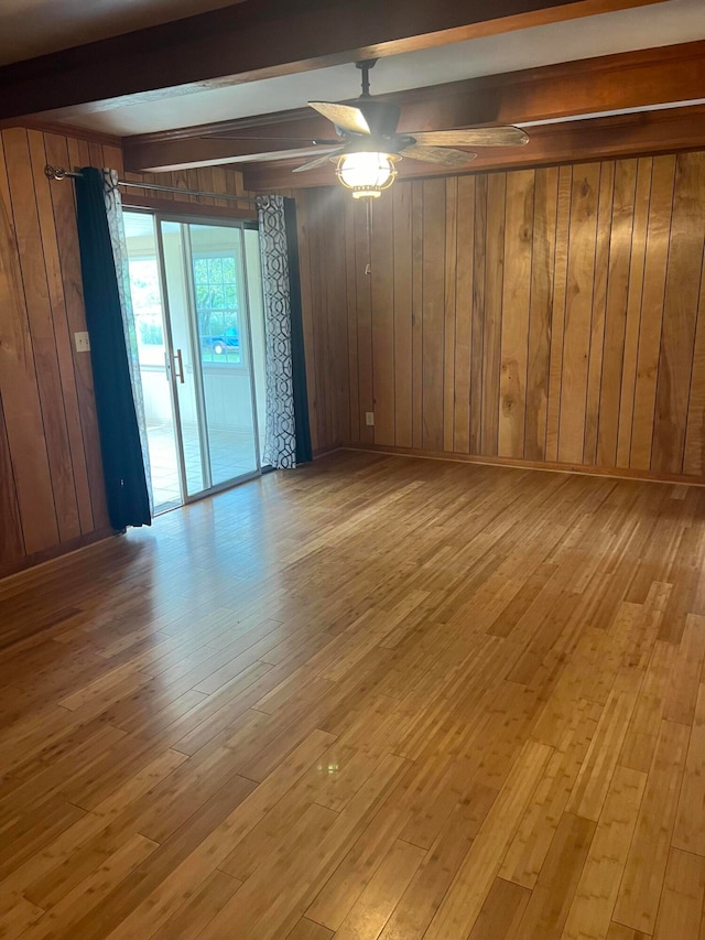 empty room with ceiling fan, beamed ceiling, wooden walls, and light hardwood / wood-style floors