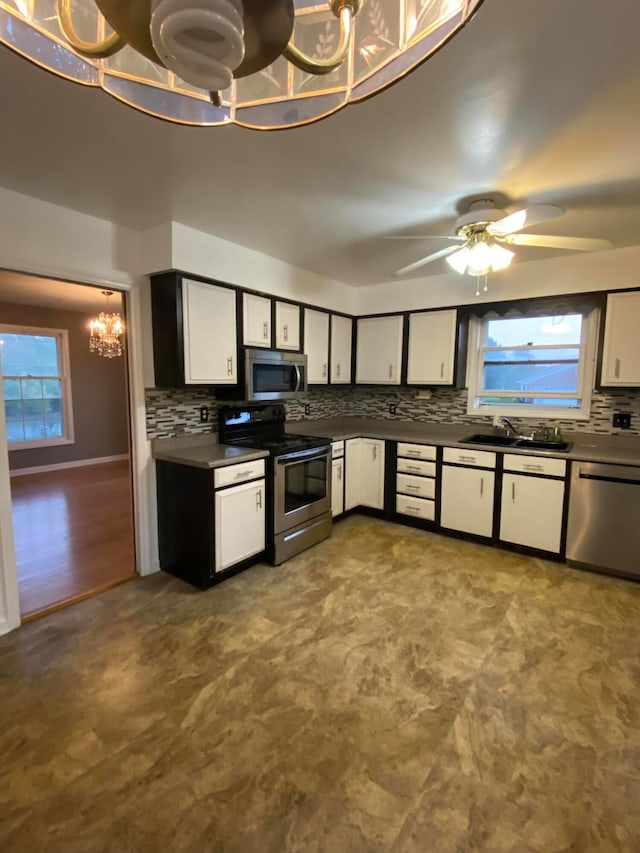 kitchen with decorative backsplash, ceiling fan with notable chandelier, sink, stainless steel appliances, and white cabinetry