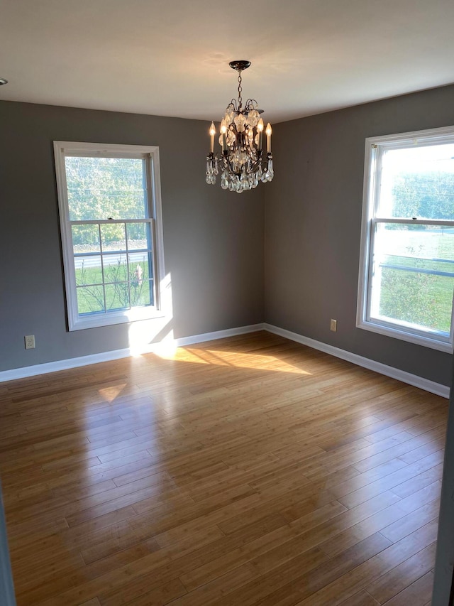 empty room with plenty of natural light, hardwood / wood-style floors, and a chandelier