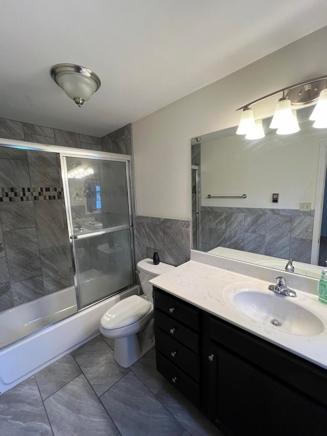 full bathroom with shower / bath combination with glass door, vanity, tile walls, and toilet