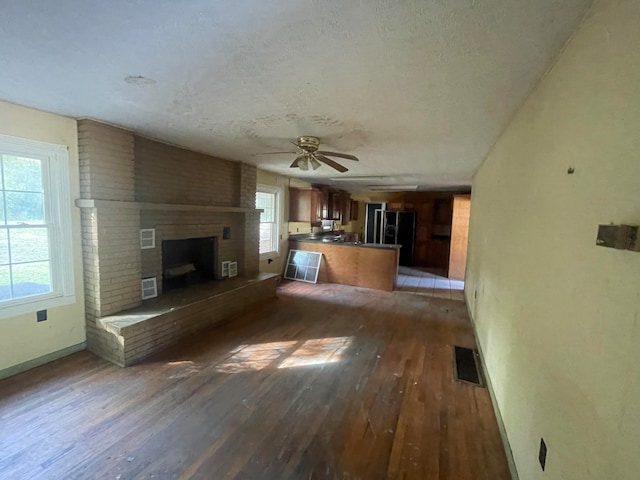 unfurnished living room with dark wood-type flooring, plenty of natural light, a brick fireplace, and ceiling fan