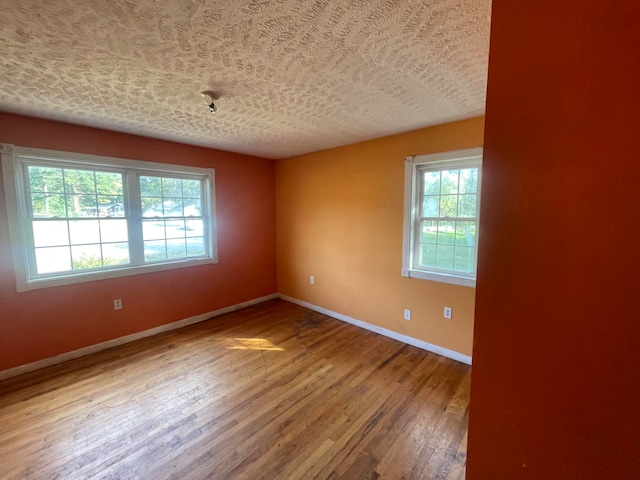 unfurnished room with hardwood / wood-style flooring, plenty of natural light, and a textured ceiling