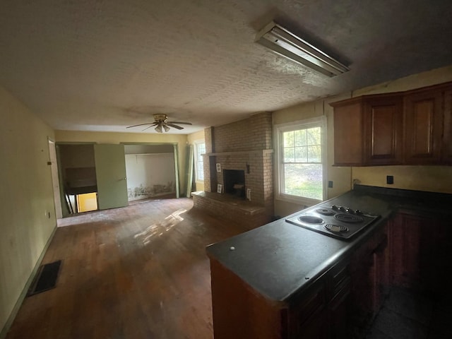 kitchen with ceiling fan, a brick fireplace, a textured ceiling, stainless steel cooktop, and dark hardwood / wood-style floors