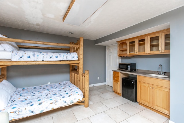 bedroom with light tile patterned floors, sink, and black fridge