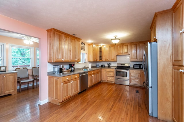 kitchen featuring tasteful backsplash, sink, light hardwood / wood-style floors, stainless steel appliances, and ceiling fan