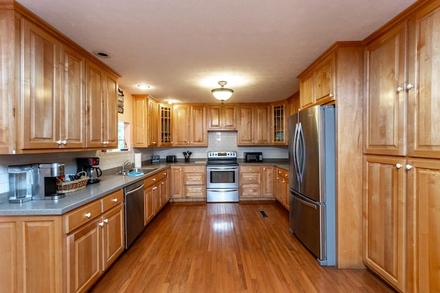 kitchen with backsplash, sink, appliances with stainless steel finishes, a textured ceiling, and light hardwood / wood-style floors