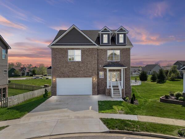 traditional-style house featuring a front yard, driveway, brick siding, an attached garage, and fence