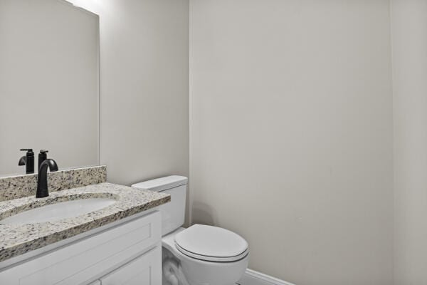 half bathroom with vanity, toilet, and baseboards