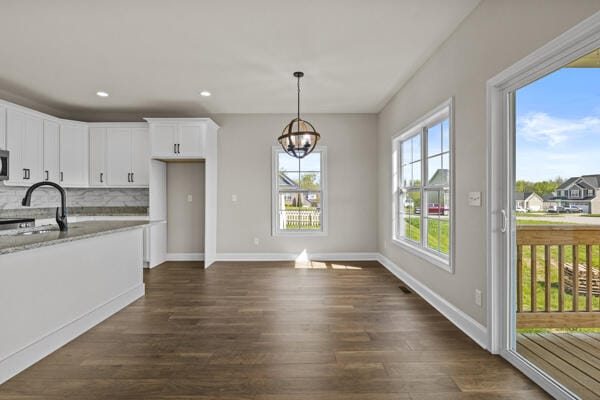 kitchen featuring a sink, dark wood-style flooring, decorative backsplash, a notable chandelier, and white cabinets