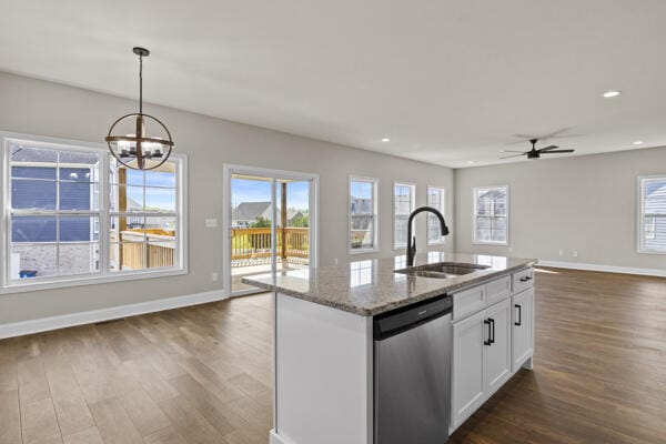 kitchen featuring stainless steel dishwasher, a sink, baseboards, open floor plan, and dark wood-style flooring