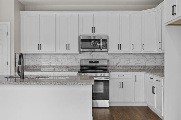 kitchen featuring appliances with stainless steel finishes, light stone countertops, white cabinets, and backsplash
