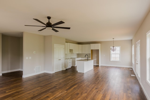 unfurnished living room with dark wood-type flooring, ceiling fan with notable chandelier, and sink