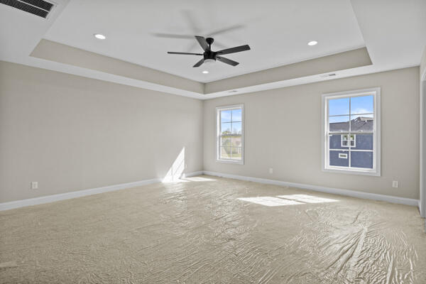 spare room featuring visible vents, a tray ceiling, baseboards, carpet floors, and a ceiling fan