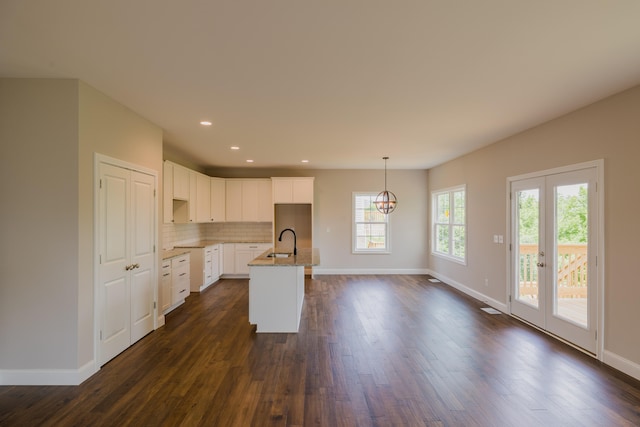 kitchen with dark hardwood / wood-style flooring, decorative light fixtures, sink, an island with sink, and white cabinets