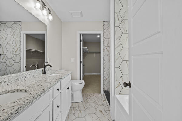 full bath featuring tile patterned floors, a tile shower, toilet, and a sink