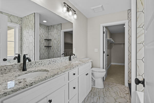 full bathroom featuring toilet, double vanity, a sink, and tiled shower