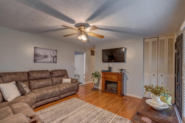 living room with light hardwood / wood-style floors, a textured ceiling, and ceiling fan