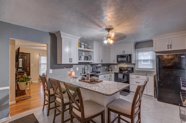 kitchen with white cabinets, ceiling fan, black appliances, light hardwood / wood-style floors, and light stone counters