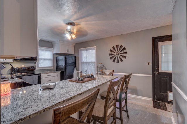 kitchen featuring a kitchen breakfast bar, black appliances, light stone countertops, white cabinetry, and ceiling fan