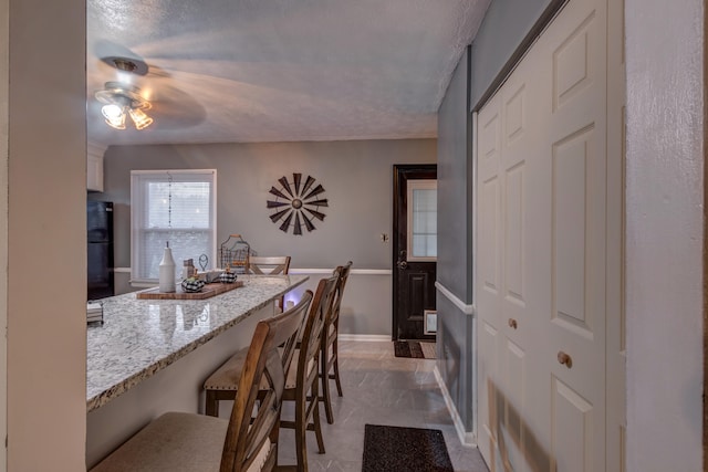 kitchen featuring a breakfast bar area, light stone countertops, a textured ceiling, and ceiling fan