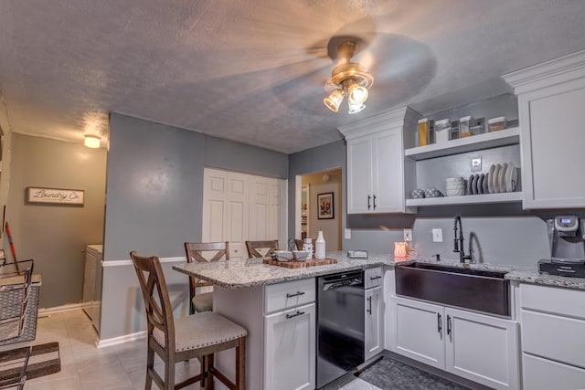 kitchen featuring white cabinets, black dishwasher, a kitchen bar, sink, and light stone counters