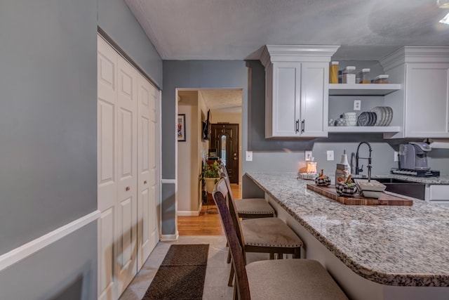 kitchen with sink, light stone countertops, a breakfast bar, white cabinets, and a textured ceiling