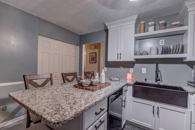 kitchen featuring kitchen peninsula, white cabinets, a breakfast bar, dishwasher, and sink