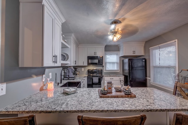 kitchen with a kitchen breakfast bar, white cabinets, black appliances, and ceiling fan